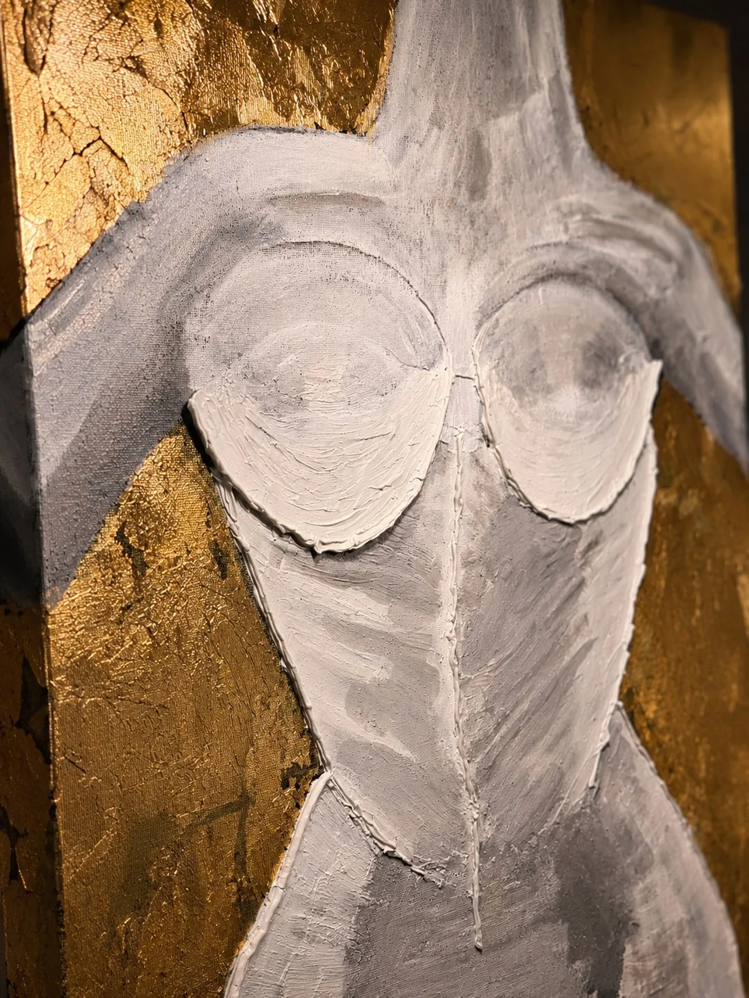 Close detail of modeling paste worked into a sculpted torso, gold leaf breaking around the edge